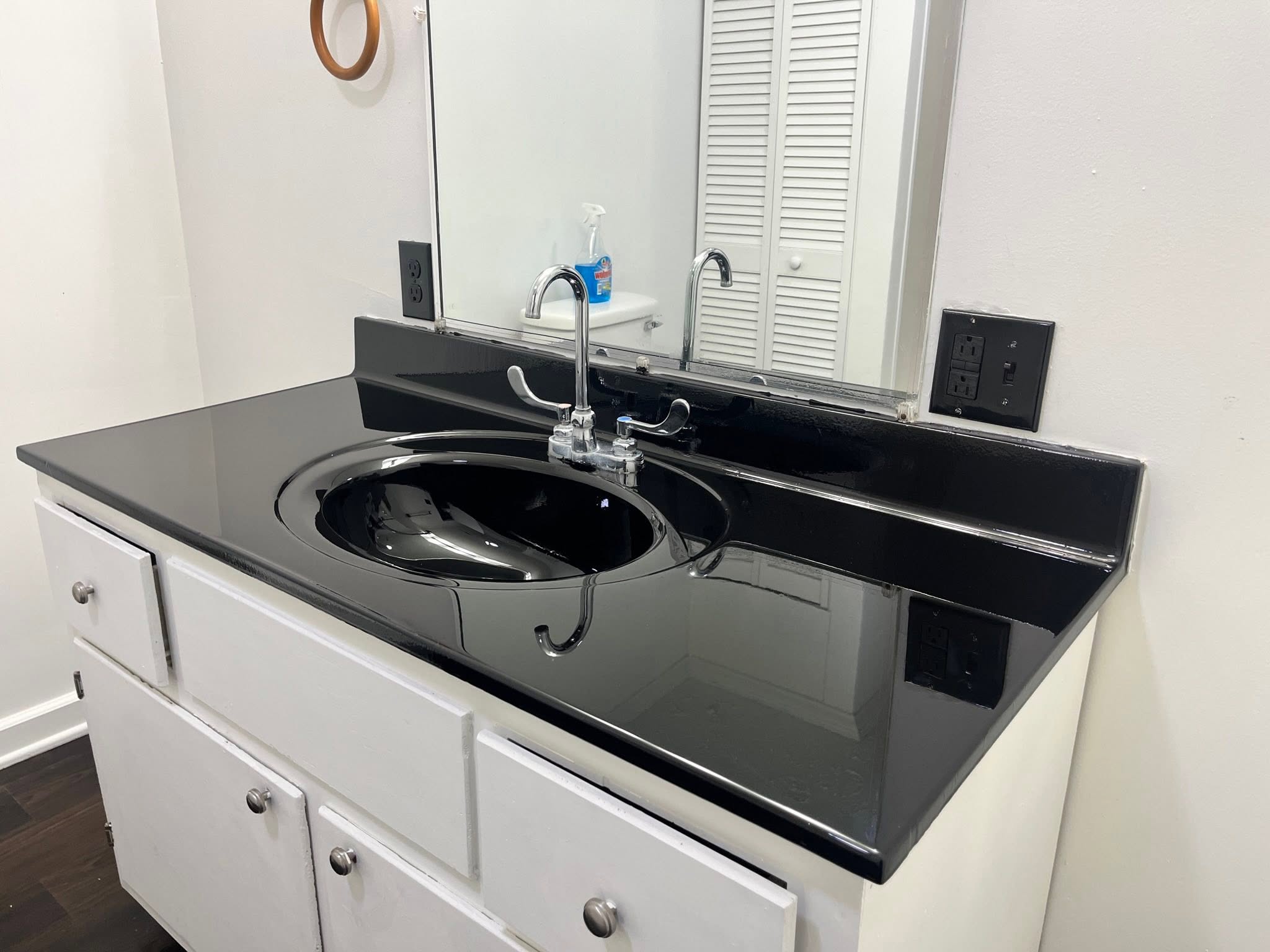 Reflective black bathroom countertop and basin with chrome faucet and white cabinets