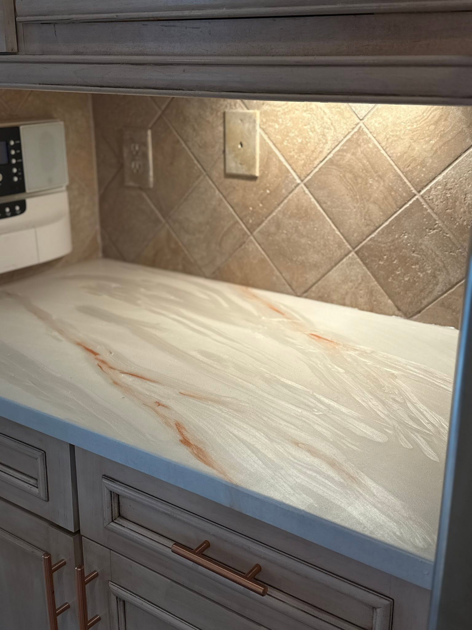 Cream epoxy counter with warm copper-colored veins, gray cabinetry and tiled backsplash